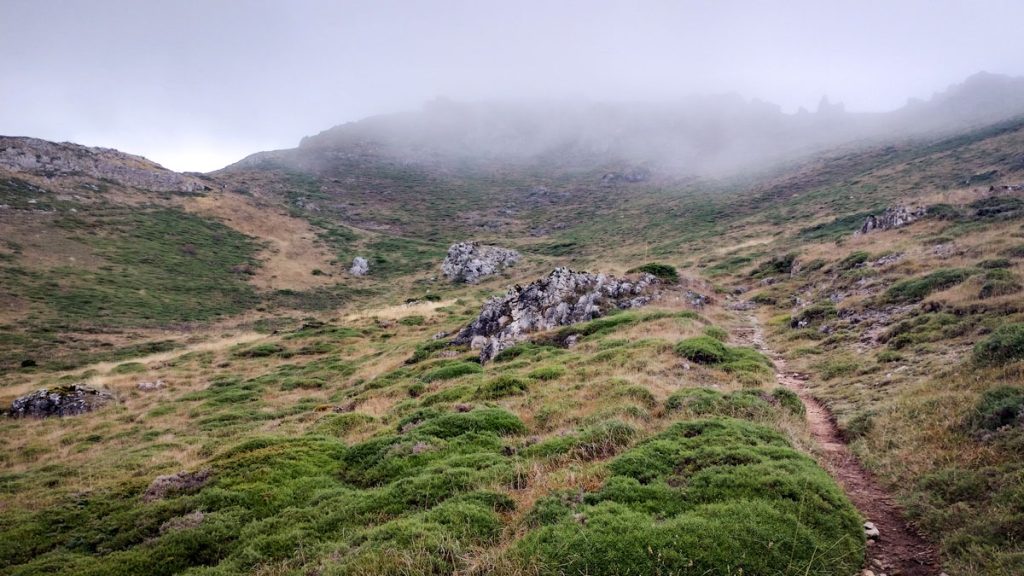 Sendero en una ladera que asciende hacia una montaña envuelta en la niebla, en el Camino del Salvador