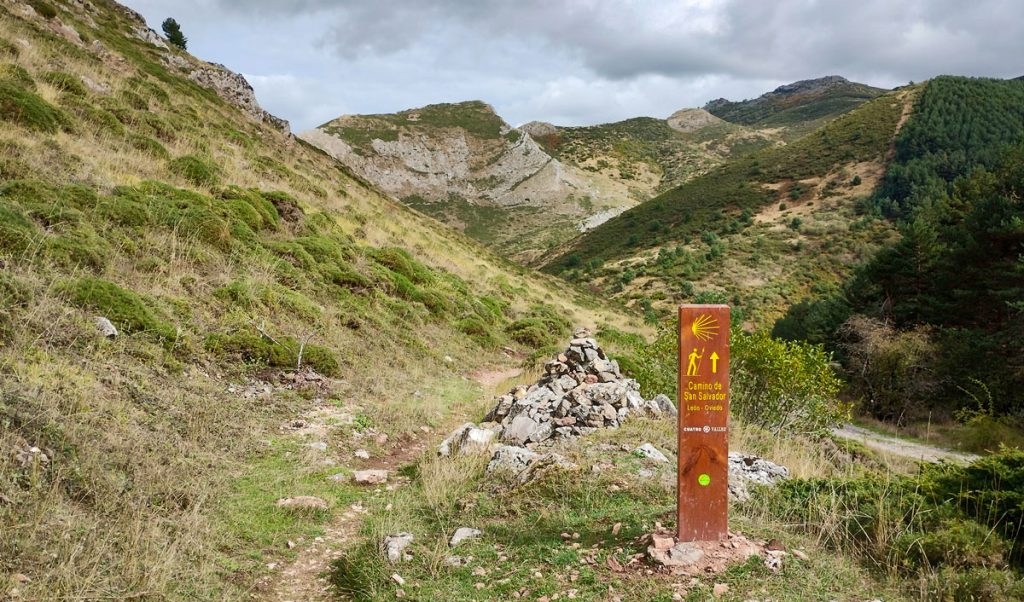 Poste de madera que señala la dirección correcta en un sendero de montaña del Camino del Salvador